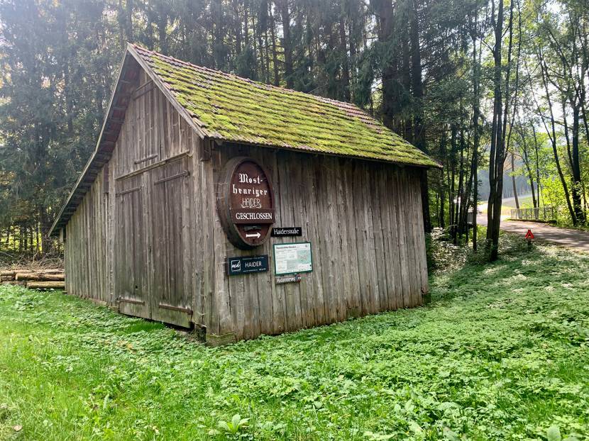 Moos bewachsene Holzhütte welche zum Mostheurigen Haider verweist